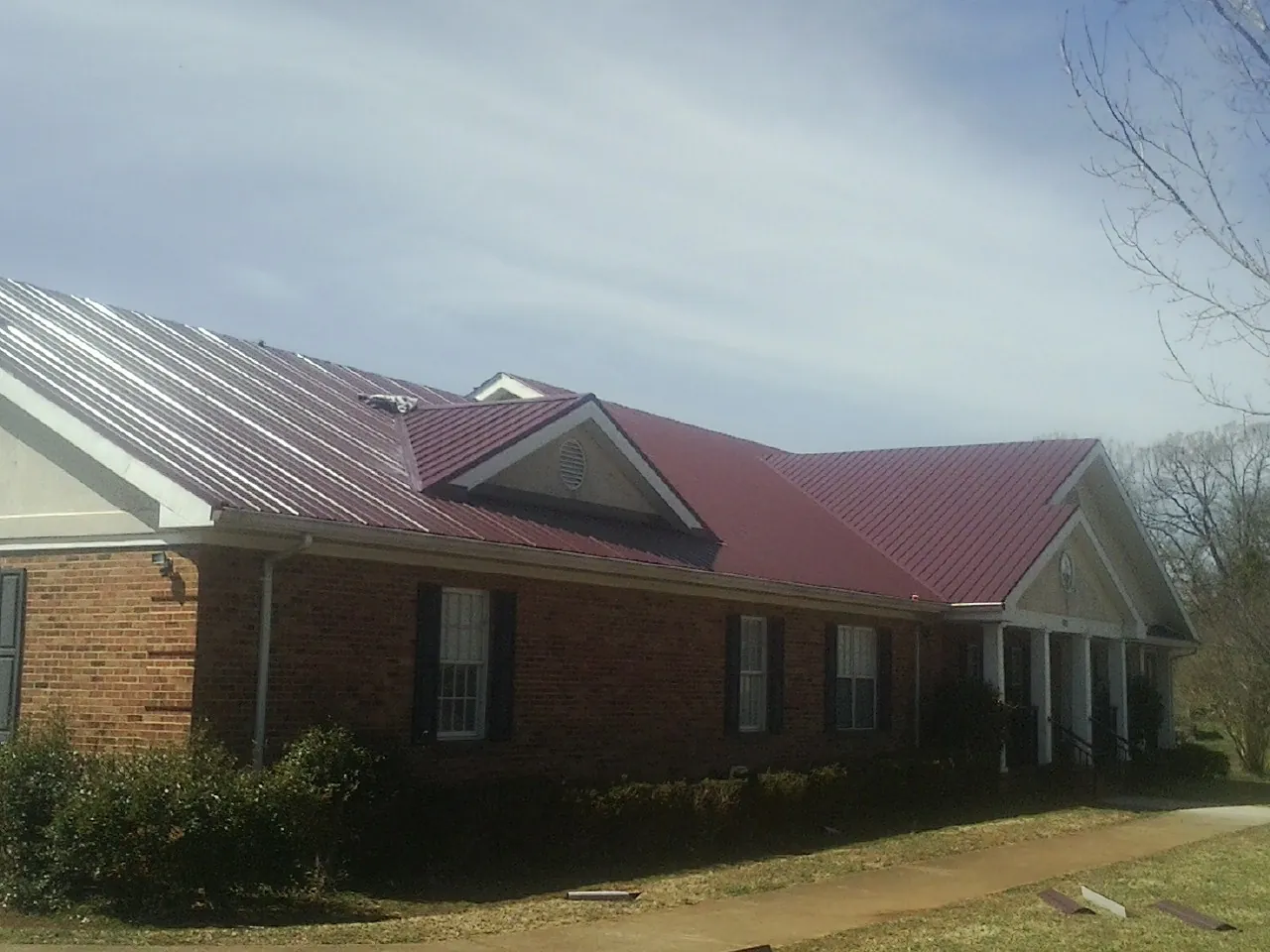 Red metal roof with gabled entries on a long brick building, from a Hail Damage Roof Repair job in Springport