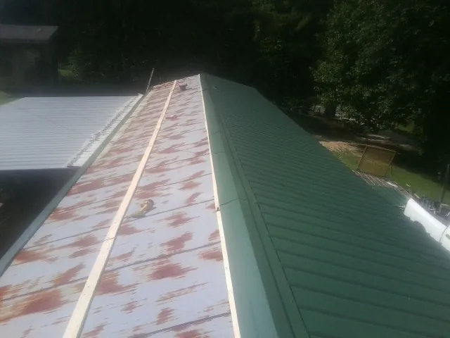 Old rusted panels beside newly installed green metal roofing — Wind Damage Roof Repair by Roofing Brothers in Springport