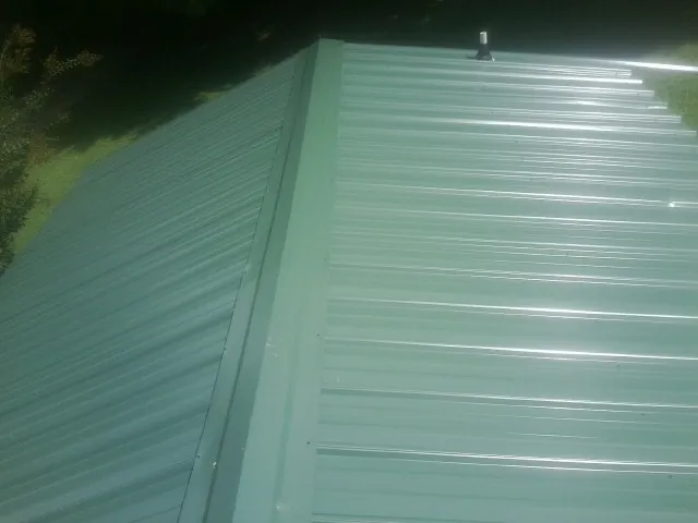 New green metal panels meeting at the ridge of a roof — Flat Roof Repair work by our crew in Springport